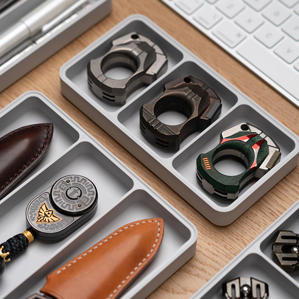 Gray compartment trays arranging rings and compact EDC pieces on a desk